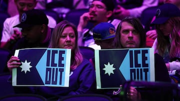 Dos aficionados de Minnesota Timberwolves sositenen carteles con el lema 'Fuera ICE'.