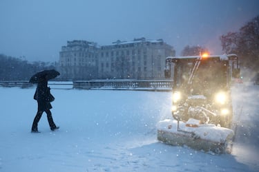 Una persona se protege de la nieve que cae bajo un paraguas junto a una máquina que limpia el suelo en la Explanada de los Inválidos cubierta de nieve en París.