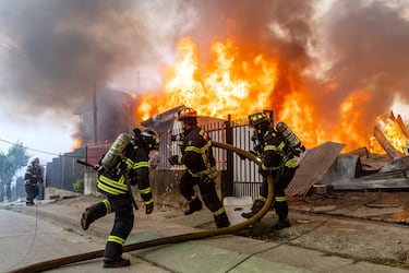 Bomberos combaten un incendio en una casa mientras los incendios forestales arden en Lirquen, Chile.