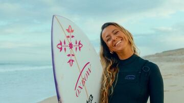 Maud Le Car con su tabla de surf y su neopreno Oxbow, sonriendo en una playa.