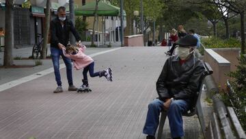 Imagen de un hombre sentado en un banco y un padre junto a su hija -todos ellos provistos de mascarillas-.