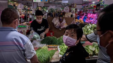(FILES) This file photo taken on June 20, 2020 shows a vendor (2nd L) selling vegetables at his stall at a market in Beijing. - A national campaign to curb mounting food waste in China is feeding speculation that the supply outlook is worse than the gover