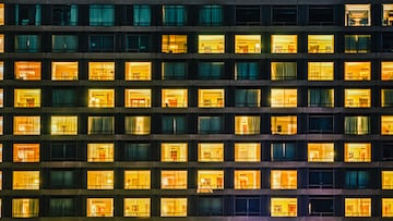 Building facade shows a windows and rooms pattern at night. The exterior features illuminated and dark living spaces with people living like neighbours in a shared communal space. Copenhagen, Denmark