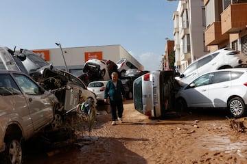 Un hombre camina junto a los coches amontonados tras las lluvias torrenciales que provocaron inundaciones, en Paiporta, Valencia.