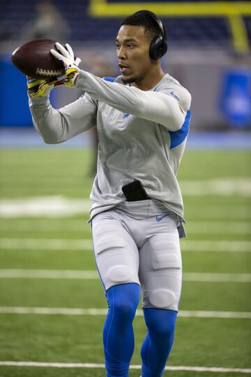 El jugador Amon-Ra St. Brown del equipo Detroit Lions calienta antes del partido escuchando música con auriculares y el móvil en la cintura del pantalón.