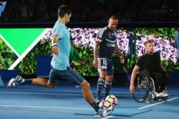 Novak Djokovic patea un balón de fútbol delante de Archie Thompson durante "una noche con Novak" en la arena de la corte de Margaret
