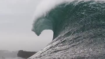 El labio de una ola gigante en Nazaré rompiendo en forma de tubo con los acantilados de esta población de Portugal al fondo.
