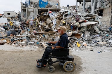 Un palestino en silla de ruedas pasa por las ruinas de edificios destruidos por los ataques israeles, en Rafah.