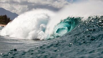 La ola de Pipeline vac&iacute;a y rompiendo, de color azul turquesa, con la playa del North Shore de Oahu (Haw&aacute;i, Estados Unidos) al fondo, con nubes y claros, durante el Billabong Pipe Masters 2018.