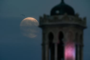 La luna llena que aparece al atardecer se alza sobre la ciudad de Izmir, Turquía.