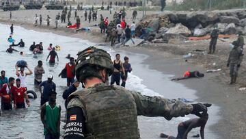 A Spanish legionnaire indicates the direction to follow to Moroccan citizens on El Tarajal beach, as they get out of the water on the Spanish side of the fence between the Spanish-Moroccan border, after thousands of Moroccans swam across this border on Mo