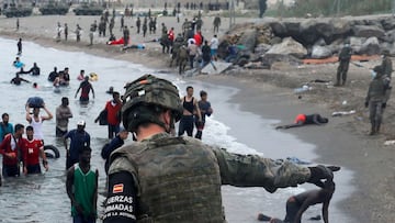 A Spanish legionnaire indicates the direction to follow to Moroccan citizens on El Tarajal beach, as they get out of the water on the Spanish side of the fence between the Spanish-Moroccan border, after thousands of Moroccans swam across this border on Mo