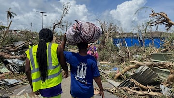 A man carries his belongings as rescue workers attempt to clear a blocked road, in the aftermath of Cyclone Chido, within Labattoir, in Mayotte.