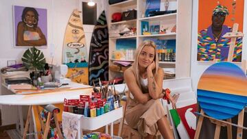 La artista canaria Kaakint, en su taller con cuadros y tablas de surf customizadas, sentada en un taburete y mirando a c&aacute;mara.