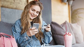 Rich girl paying for everyone, celebrating promotion at work, sitting in fancy cafe wearing stylish outfit, holding smartphone and credit card, talking casually while making payment via internet app.