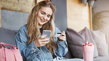 Rich girl paying for everyone, celebrating promotion at work, sitting in fancy cafe wearing stylish outfit, holding smartphone and credit card, talking casually while making payment via internet app.