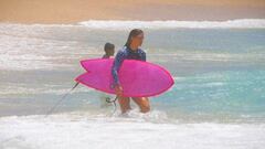 La surfista vasca Garazi Sanchez entrando al agua en una playa de M&eacute;xico con su tabla de surf twinfin de color rosa.