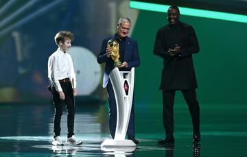 Didier Deschamps y un pequeño aficionado francés llevan, como últimos campeones del mundo, el trofeo al escenario.