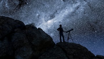 Hombre viendo estrellas junto a un telescopio en el desierto.