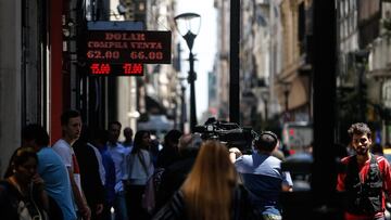 Transeúntes caminan bajo un tablero que indica el precio del dólar en compra y venta respecto al peso argentino en Buenos Aires (Argentina). EFE/ Juan Ignacio Roncoroni/Archivo