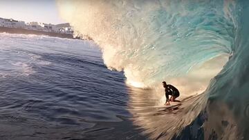 El surfista canario Manuel Lezcano surfeando un tubo de izquierdas en El Quemao (La Santa, Lanzarote, Islas Canarias), con la población y sus casas blancas al fondo.