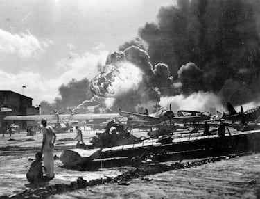 Explosión en la Estación Aérea Naval de la isla Ford, Pearl Harbor, durante el ataque japonés. Marineros entre los restos observan la explosión del USS Shaw al fondo. El acorazado USS Nevada también se ve al fondo, con la proa hacia la izquierda.