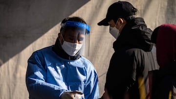 A health worker (L) offers hand sanitising gel for people queueing for PCR (polymerase chain reaction) tests at a Covid-19 coronavirus testing centre in Seoul on December 8, 2021. (Photo by Anthony WALLACE / AFP)
