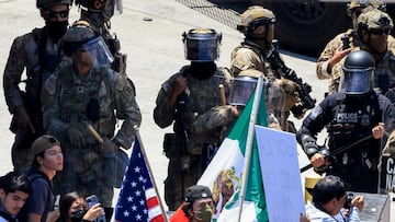 Oficial de policía y miembros del Ejército de EE. UU. junto a manifestantes que ondean banderas de Estados Unidos y México en Los Ángeles.