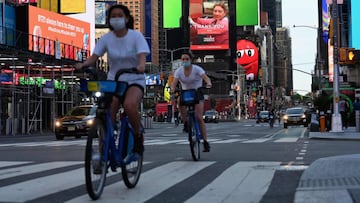 (FILES) In this file photo taken on May 27, 2020 people wearing a facemasks ride their bikes through Times Square in New York City, amid the novel coronavirus pandemic. - New York, the US city worst-hit by the coronavirus, is "on track" to start