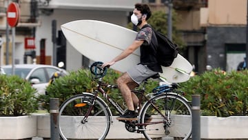 GRAFCVA4885. VALENCIA, 09/05/2020.-Un surfista protegido con mascariilla carga su tabla en bici hacia la playa de la Malvarrosa, en Valencia, hoy quincuagésimo sexto día del estado de alarma. EFE/ Juan Carlos Cárdenas