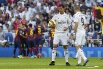 Lo jugadores del Real Madrid, Cristiano Ronaldo,iz. y Karim Benzema, con el balon mientras los jugadores del Barcelona celebran el primer gol del partido correspondiente a la novena jornada de Liga de Primera División que disputan en el estadio Santiago Bernabéu.
