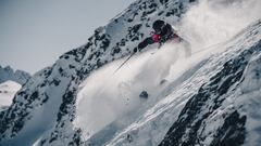 Un esquiador bajando por una monta&ntilde;a y levantando nieve. 