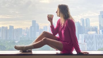 Maya Gabeira tom&aacute;ndose un caf&eacute; en calcetines y un vestido rosa con los rascacielos de Jakarta (Indonesia) de fondo. 