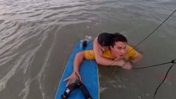 Bruno Lobo con una mujer en la espalda apoyado en su tabla de kitesurf en la playa de Sao Luis, Brasil, el 10 de enero del 2025.
