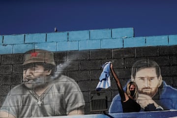A woman reacts in front of a mural depicting the late soccer legend Diego Armando Maradona and soccer player Lionel Messi near Bella Vista cemetery, where Maradona will be buried, on the outskirts of Buenos Aires, Argentina, November 26, 2020. REUTERS/Ues
