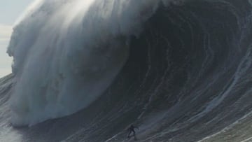 Mason Barnes surfeando una ola gigantesca en Nazar&eacute;, rompiendo y haciendo forma de tubo, con &eacute;l en la parte baja y visto desde el agua. 