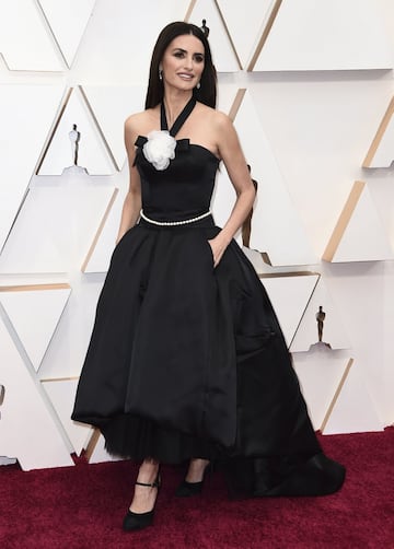 Penélope Cruz posó con un vestido de Chanel modelo negro satinado. Más largo por detrás y corto por delante con tul., salones anudados al bolsillo, una flor blanca en el escote, cinturon de bolitas y escote a la espalda.