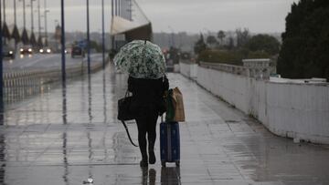 una persona camina bajo la lluvia con un paraguas y una maleta. En Sevilla (Andalucía, España), a 04 de diciembre de 2020.