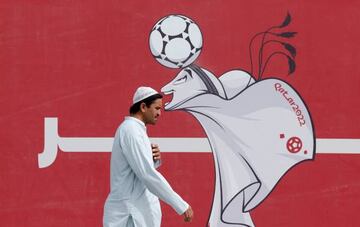 A man walks past a poster of the Qatar 2022 mascot La'eeb in Doha