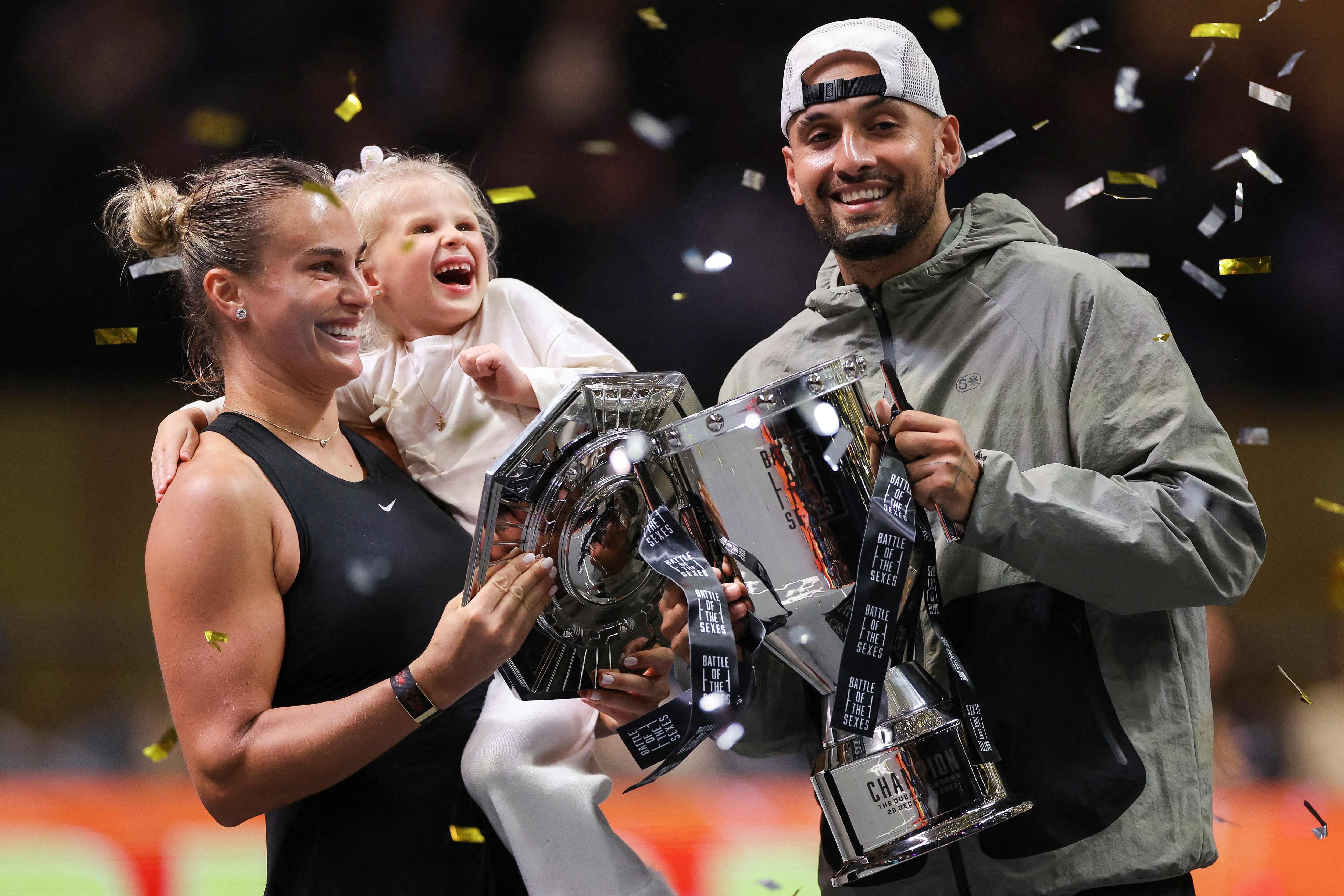 Belarus' Aryna Sabalenka (L), her goddaughter Nicole, and Australia's Nick Kyrgios celebrate with trophies at the end of the Battle of the Sexes exhibition tennis match in Dubai on December 28, 2025. (Photo by Amr Alfiky / POOL / AFP)
