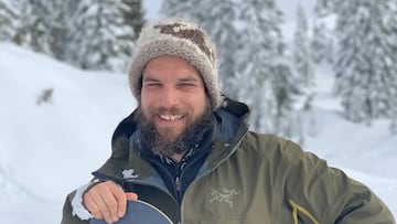 Jeff Keenan, snowboarder profesional, sonriendo con su tabla de snowboard en la nieve.