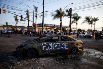 Un autom¨®vil quemado, con un insulto al ICE escrito en aerosol, reposa en una calle en Paramount, California. Debido a que la situaci¨®n se elev¨® en cuanto a violencia, Donald Trump anunci¨® el env¨ªo de 2,000 agentes de la Guardia Nacional, pese a que ni la alcaldesa de Los ?ngeles, Karen Bass, ni el gobernador de California, Gavin Newsom, solicitaron la intervenci¨®n. Ello llevo a la administraci¨®n de Newsom a presentar una demanda contra el gobierno de Trump, por exceder su autoridad.