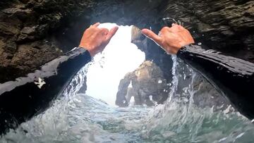 Los brazos y manos de Guillermo Carracedo realizando el saludo surfero del shaka bajo los arcos de roca de la playa de las Catedrales (Galicia, España).