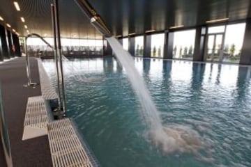 Piscina cubierta de la residencia del primer equipo del Real Madrid en la Ciudad Deportiva de Valdebebas. El edificio, destinado a que las concentraciones y las horas de convivencia entre los futbolistas y el cuerpo técnico sean lo más amenas posible, cuenta con cincuenta y siete habitaciones individuales. Personalizadas todas ellas con el nombre de su inquilino, se agrupan en dos de las tres plantas del inmueble, 32 en la intermedia y 25 en la más alta. Similares en su diseño salvo la del entrenador, que tiene además un aparte para trabajar y reunirse, las estancias están equipadas con lo último en tecnología y contienen terrazas que comparten cada dos personas.