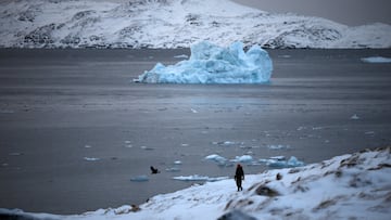 A person walks on the shore as a small iceberg floats in the sea near Nuuk, Greenland, February 4, 2026. REUTERS/Stoyan Nenov