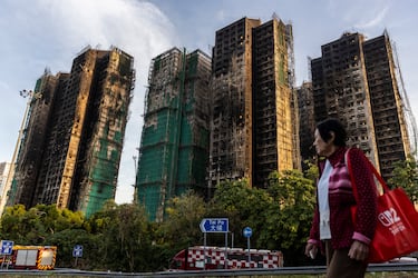 Una mujer camina junto a edificios residenciales dañados por el incendio en el Tribunal Wang Fuk, en el distrito de Tai Po.