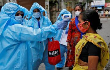 A health worker wearing protective gear uses an infrared thermometer to check the temperature of a woman.