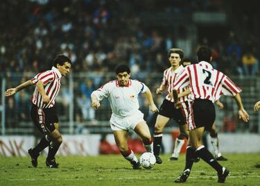 Aquel Sevilla de la 92-93 fue también el de Diego Armando Maradona (Lanús, 1960-Dique Luján, 2020) al que Bilardo insistió en fichar tras su sanción de 15 meses por doping en el Nápoles. Andaba convencido el entrenador argentino de que su sociedad con el Pelusa obraría en Nervión un milagro parecido o superior al que habían armado en México-86 como líderes de la albiceleste, con algún título o al menos clasificación europea de por medio. El fichaje, autorizaciones judiciales y 750 millones de pesetas de la época aparte, fue duro como un parto. Diego llegó en octubre, brilló a ratos en el césped del Sánchez Pizjuán y con anécdotas como la de darle pataditas a una naranja antes de sacar un córner en el Sánchez Pizjuán. Se habló más de él en el cuché gracias a sus andanzas fuera del estadio, entre ellas la de irse con Argentina sin permiso. ¡Venga ya!, mantiene algún conocido cuando se critica el carácter excéntrico del Pelusa, también a la sombra del Guadalquivir. Acabó peleado con Bilardo y con la directiva de Luis Cuervas. 