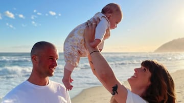 Jamie Civil, su pareja Courtney y su hija Lenni en la playa, vestidos de blanco, con olas al fondo. 