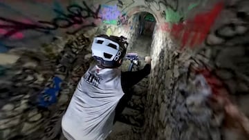 El piloto de MTB Antoni Villoni bajando con su bici Commencal por las escaleras de uno de los t&uacute;neles de las Catacumbas de Par&iacute;s, llenos de graffiti, equipado &uacute;nicamente con una luz frontal. 